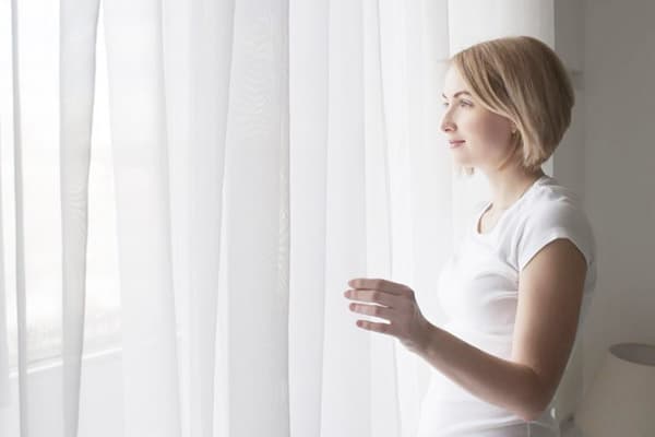 Fille à la fenêtre avec un rideau blanc