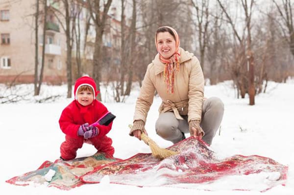 Femme et enfant nettoyant un tapis dans la neige