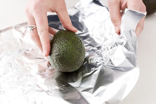 Une femme enveloppe un avocat dans du papier aluminium