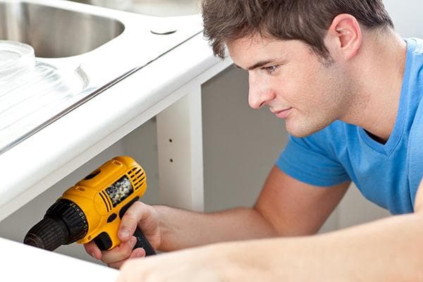 Un homme répare un meuble sous l’évier