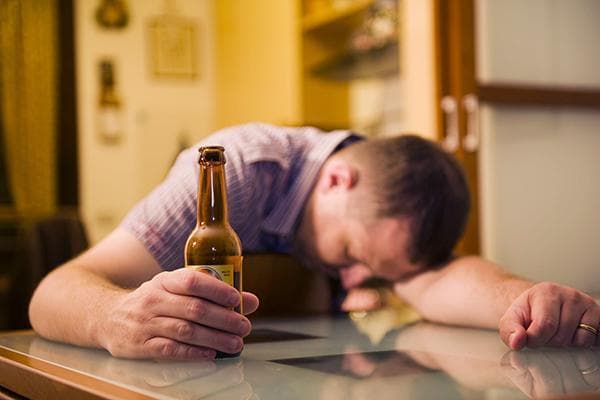 Homme ivre avec une bouteille de bière à table