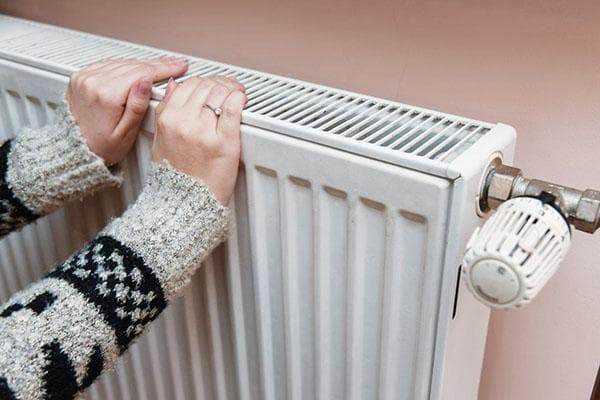 Une femme se réchauffe les mains sur le radiateur